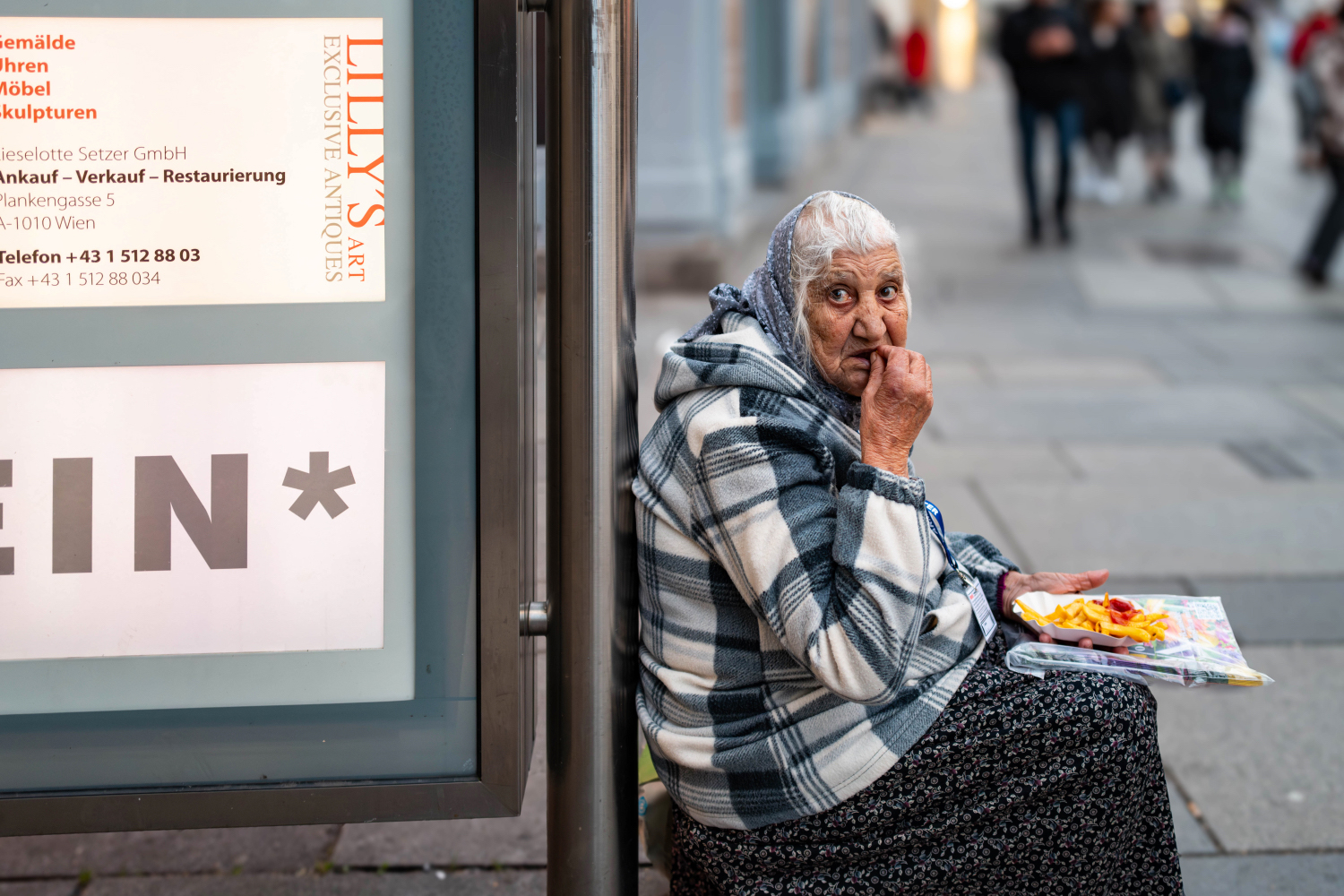 Oudere dame eet een patatje, zittend op straat